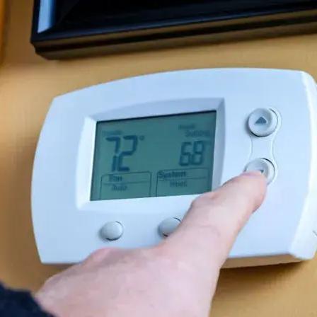 Finger pressing a button on a wall thermostat showing 72 degrees