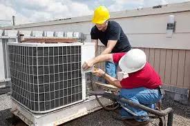 Two technicians in hard hats servicing a rooftop air conditioning unit