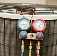 Refrigerant gauge set hanging on the grille of an outdoor air conditioning unit