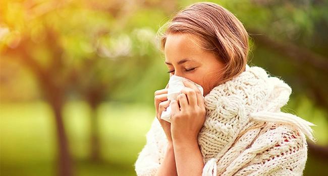Woman in a knit sweater blowing her nose outdoors in spring