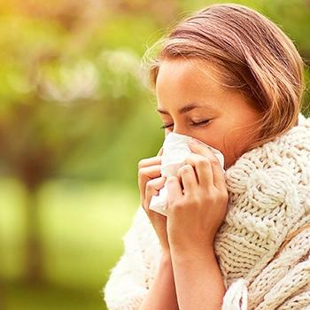 Woman in a knit sweater blowing her nose outdoors in spring