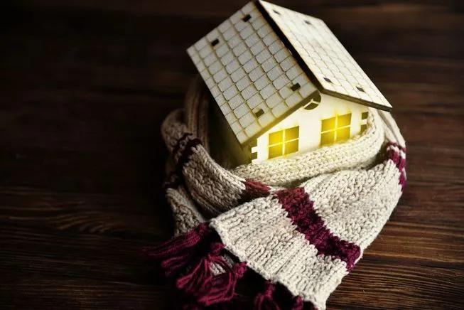 Small wooden house model wrapped in a knitted scarf with its windows lit