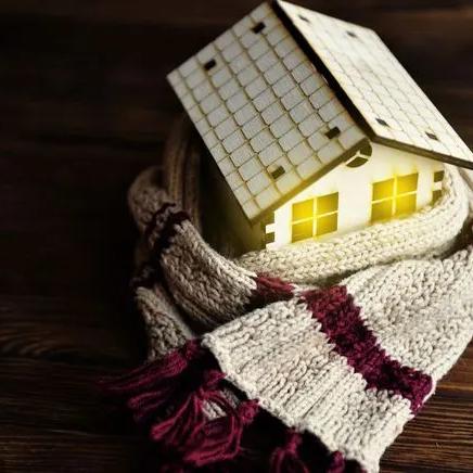 Small wooden house model wrapped in a knitted scarf with its windows lit