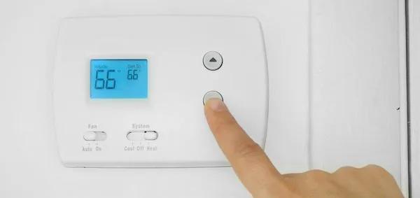 Finger pressing a button on a wall thermostat showing 66 degrees
