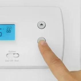 Finger pressing a button on a wall thermostat showing 66 degrees