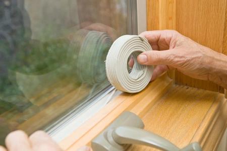 Hands applying weatherstripping tape to a window frame