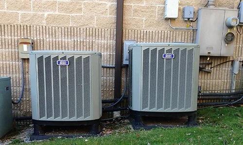 Two outdoor air conditioning units against a brick wall