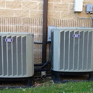 Two outdoor air conditioning units against a brick wall