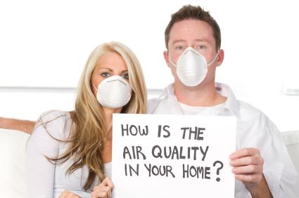 Couple wearing dust masks holding a sign that reads "How is the air quality in your home?"