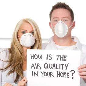 Couple wearing dust masks holding a sign that reads "How is the air quality in your home?"