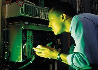 Technician inspecting equipment inside a control cabinet under green light