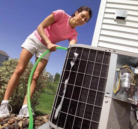 Woman rinsing the coils of an outdoor air conditioning unit with a garden hose