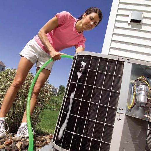Woman rinsing the coils of an outdoor air conditioning unit with a garden hose