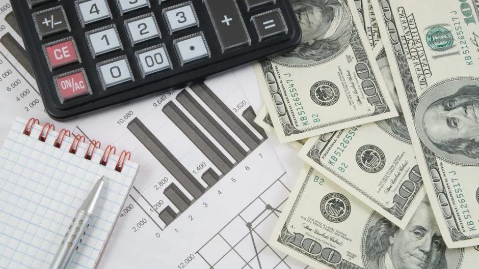 Calculator, notebook, bar chart and US dollar bills on a desk