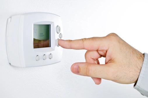Finger pressing a button on a white wall thermostat