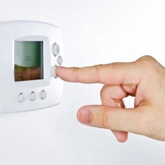 Finger pressing a button on a white wall thermostat