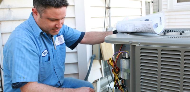 Technician in a blue uniform servicing an outdoor air conditioning unit