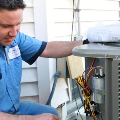 Technician in a blue uniform servicing an outdoor air conditioning unit