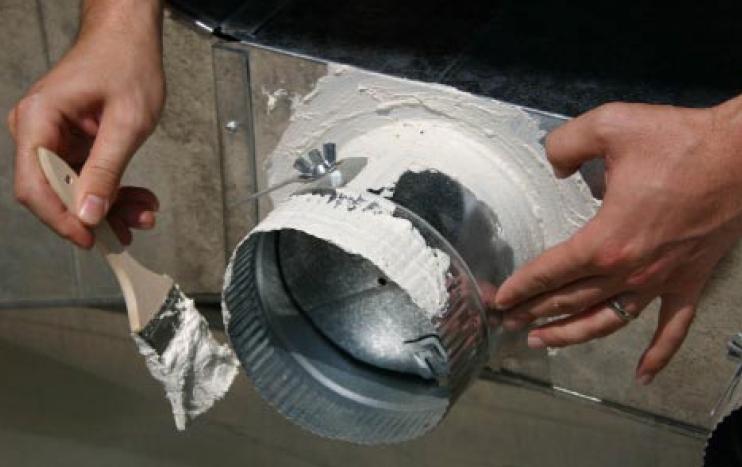 Hands brushing mastic sealant onto a metal duct collar