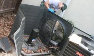 Technician working inside an outdoor air conditioning unit with its top panel removed
