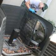 Technician working inside an outdoor air conditioning unit with its top panel removed