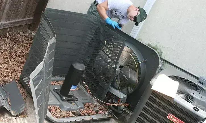 Technician working inside an outdoor air conditioning unit with its top panel removed