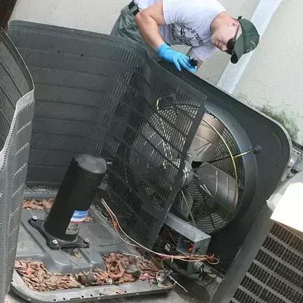 Technician working inside an outdoor air conditioning unit with its top panel removed