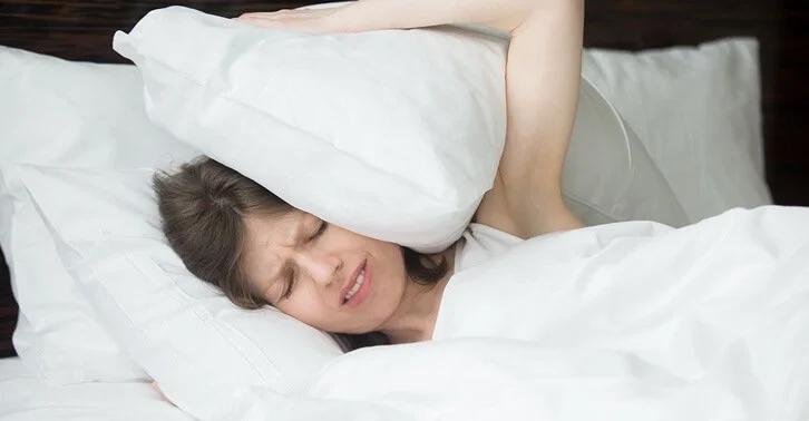 Woman in bed covering her ears with a pillow