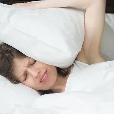 Woman in bed covering her ears with a pillow