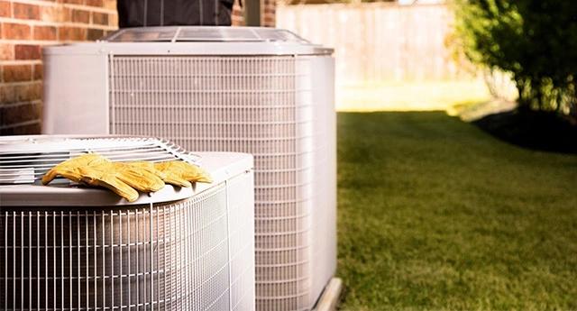 Outdoor air conditioning unit beside a brick house with a pair of work gloves resting on top