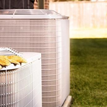 Outdoor air conditioning unit beside a brick house with a pair of work gloves resting on top