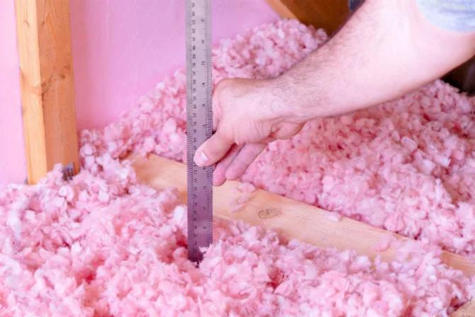 Ruler measuring the depth of pink fiberglass insulation in an attic