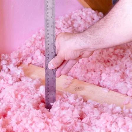Ruler measuring the depth of pink fiberglass insulation in an attic