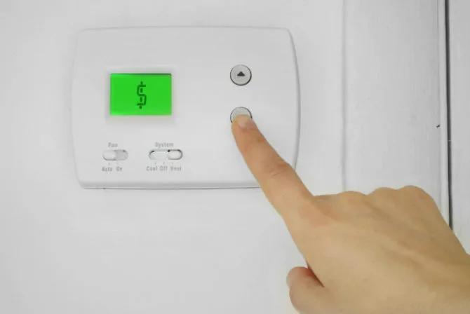 Finger pressing a button on a wall thermostat with a green display
