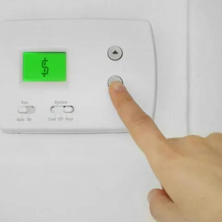 Finger pressing a button on a wall thermostat with a green display