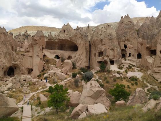 Fairy-chimney rock formations riddled with carved cave-dwelling entrances at Zelve Open Air Museum, Cappadocia, with a visitor staircase winding through the valley.
