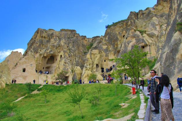Rock-cut Byzantine church facades and cave dwellings carved into the tuff cliffs of Göreme Open Air Museum, Cappadocia, with visitors on the path below.