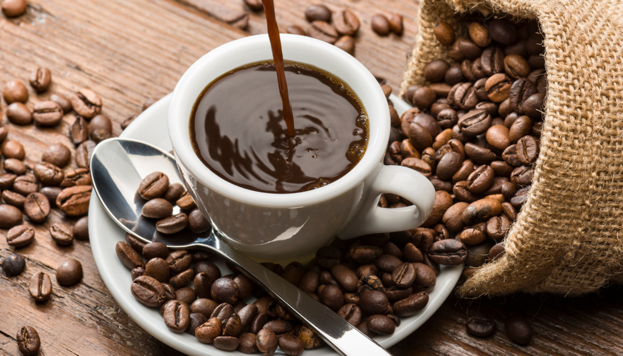 coffee being poured into a cup surrounded by coffee beans