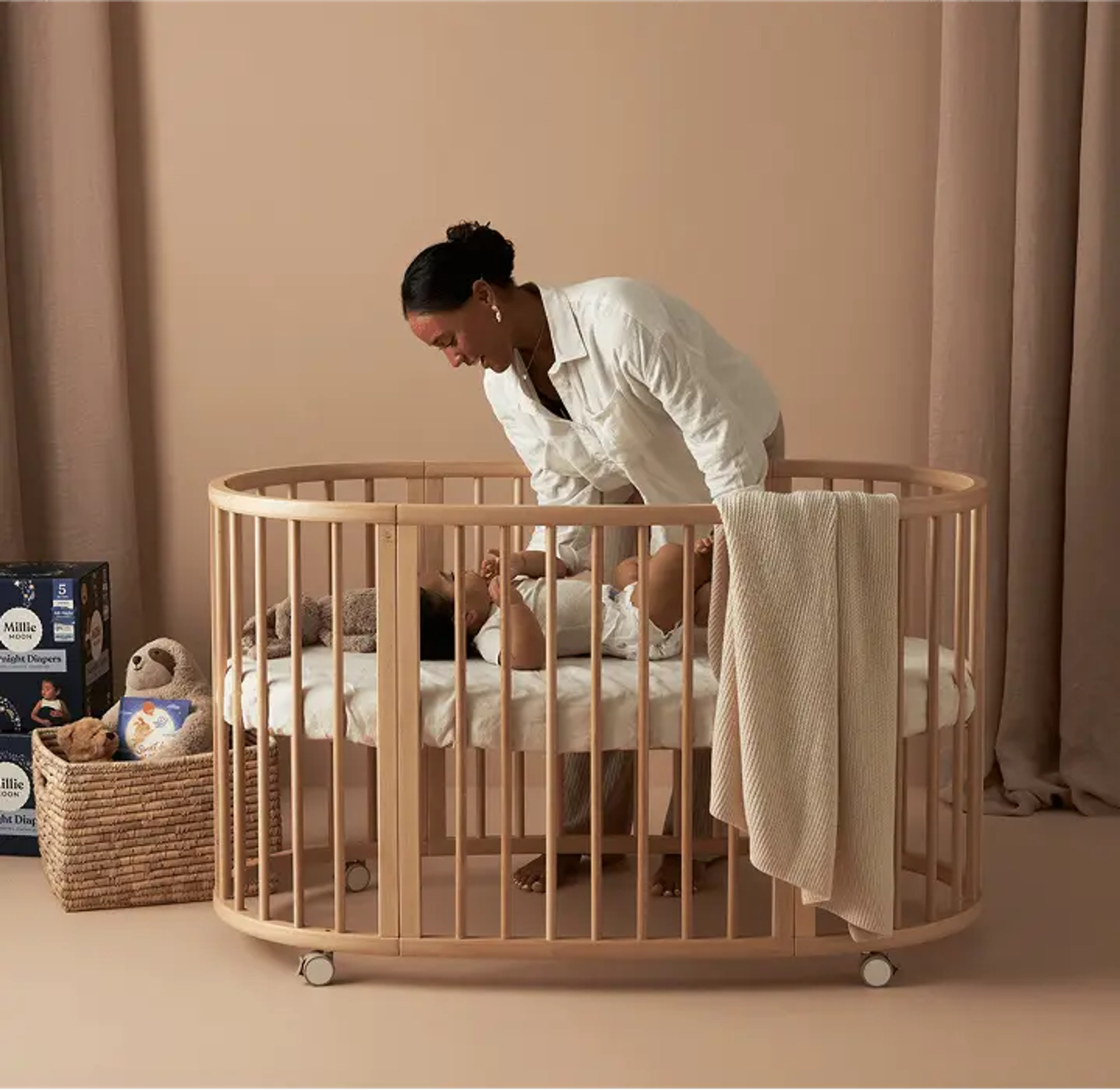 Parent settling a baby into a crib beside a pack of Millie Moon Overnight Diapers