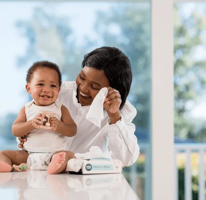 Parent using a Millie Moon Sensitive Wipe to clean a smiling baby's hands
