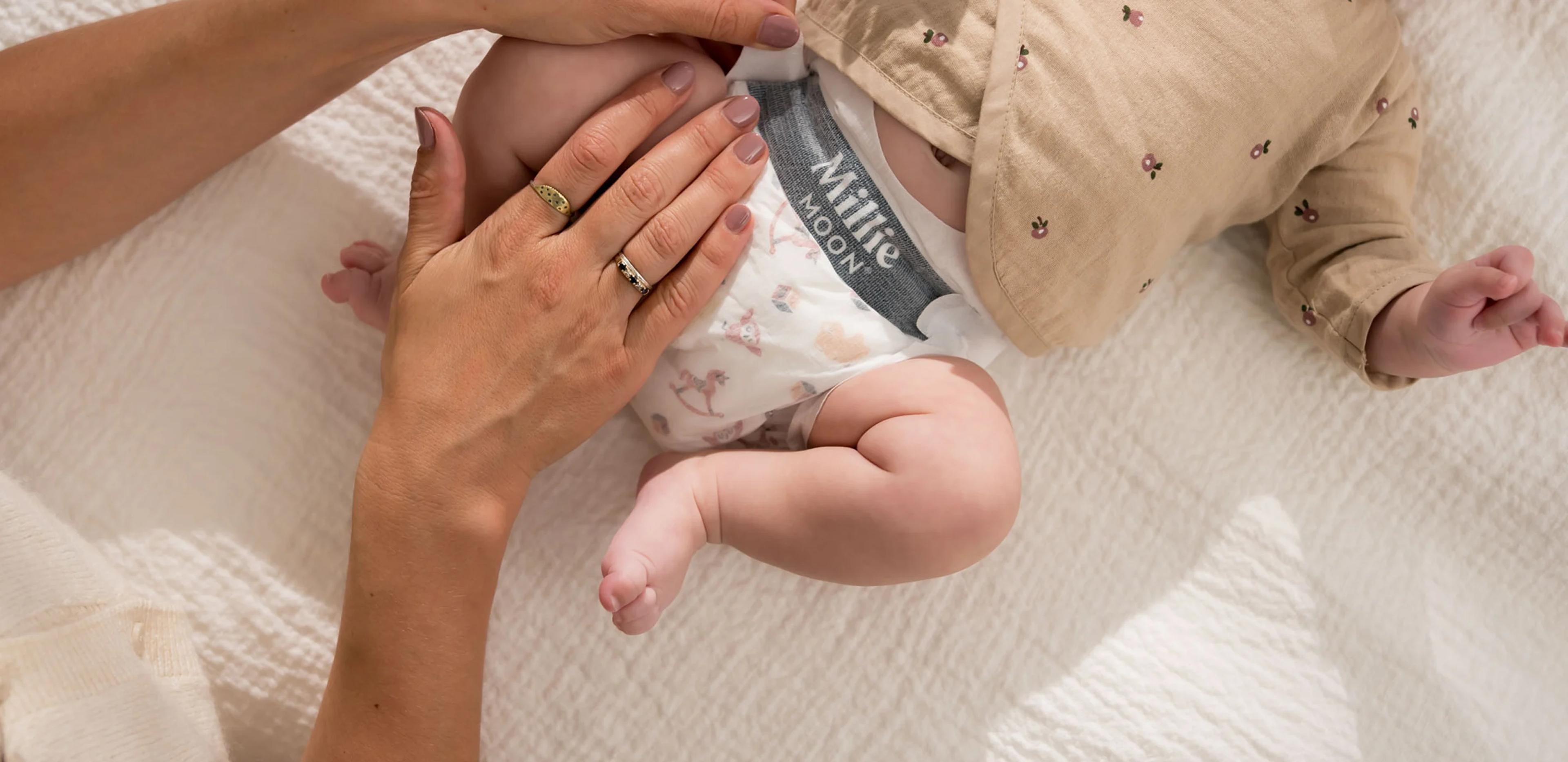 Parent changing a baby into a Millie Moon Luxury Diaper on a white quilt