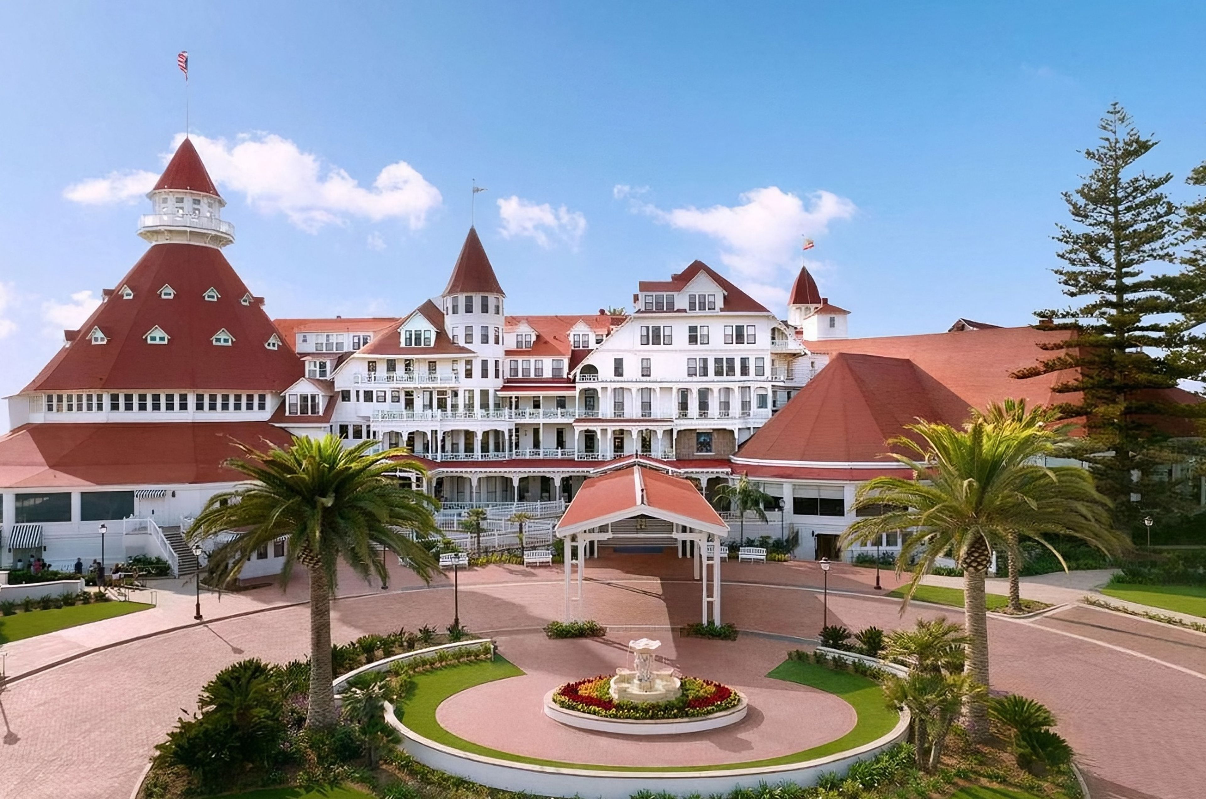 The white timber facade and red conical turrets of Hotel del Coronado in San Diego, with palms around a fountain in the circular driveway