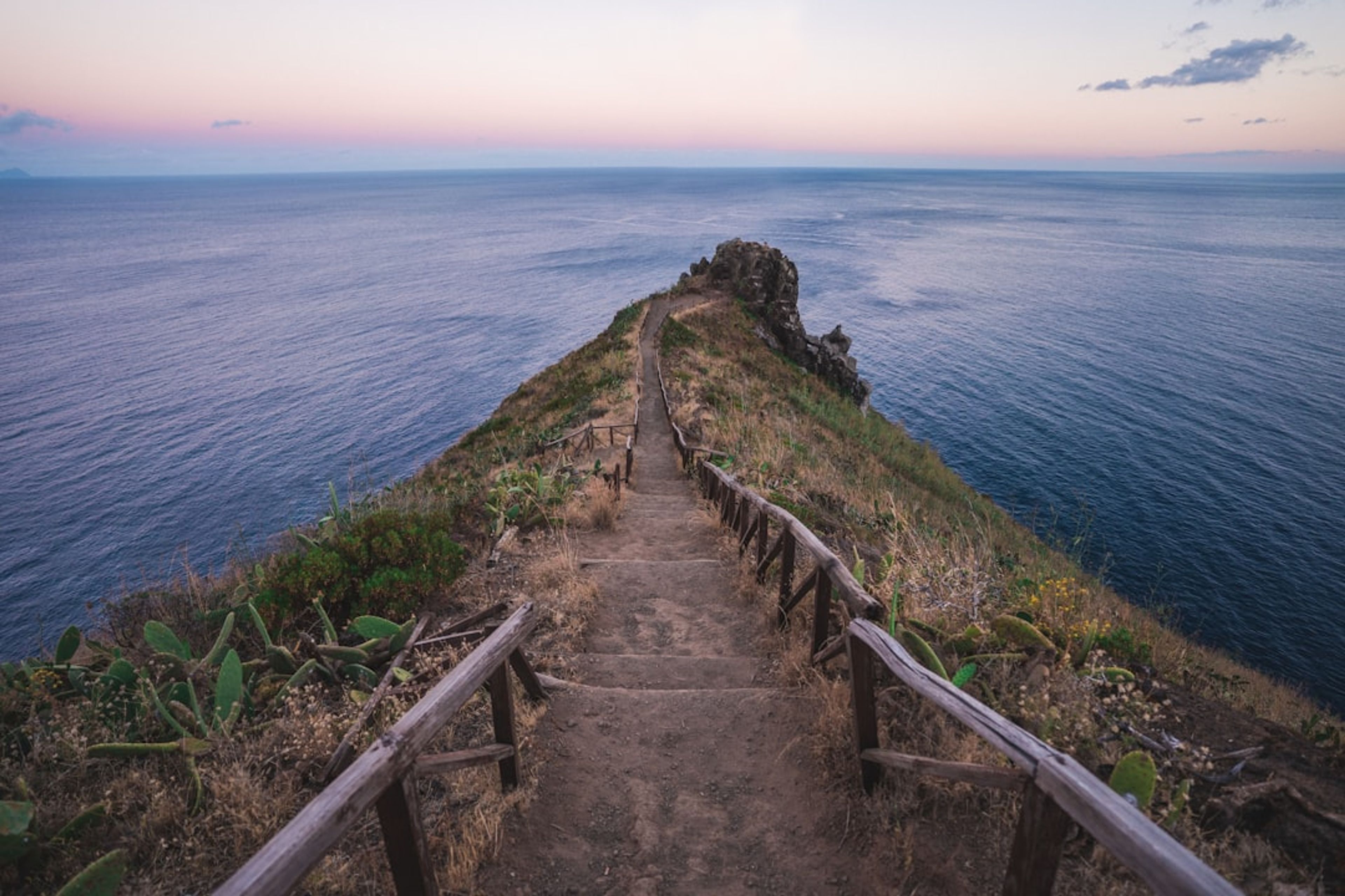 Coastal hiking trail with wooden railings running out along a clifftop headland above the sea at dusk