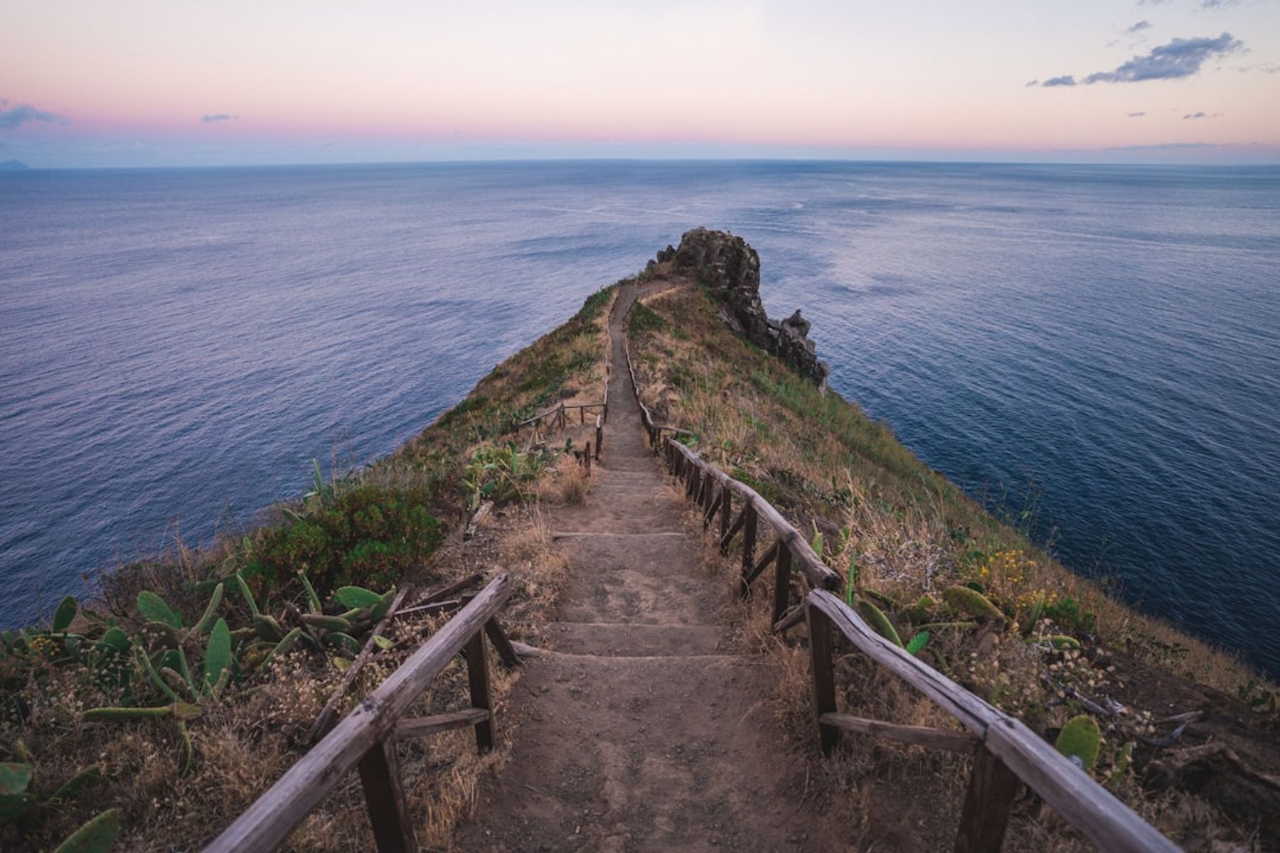 Coastal hiking trail with wooden railings running out along a clifftop headland above the sea at dusk