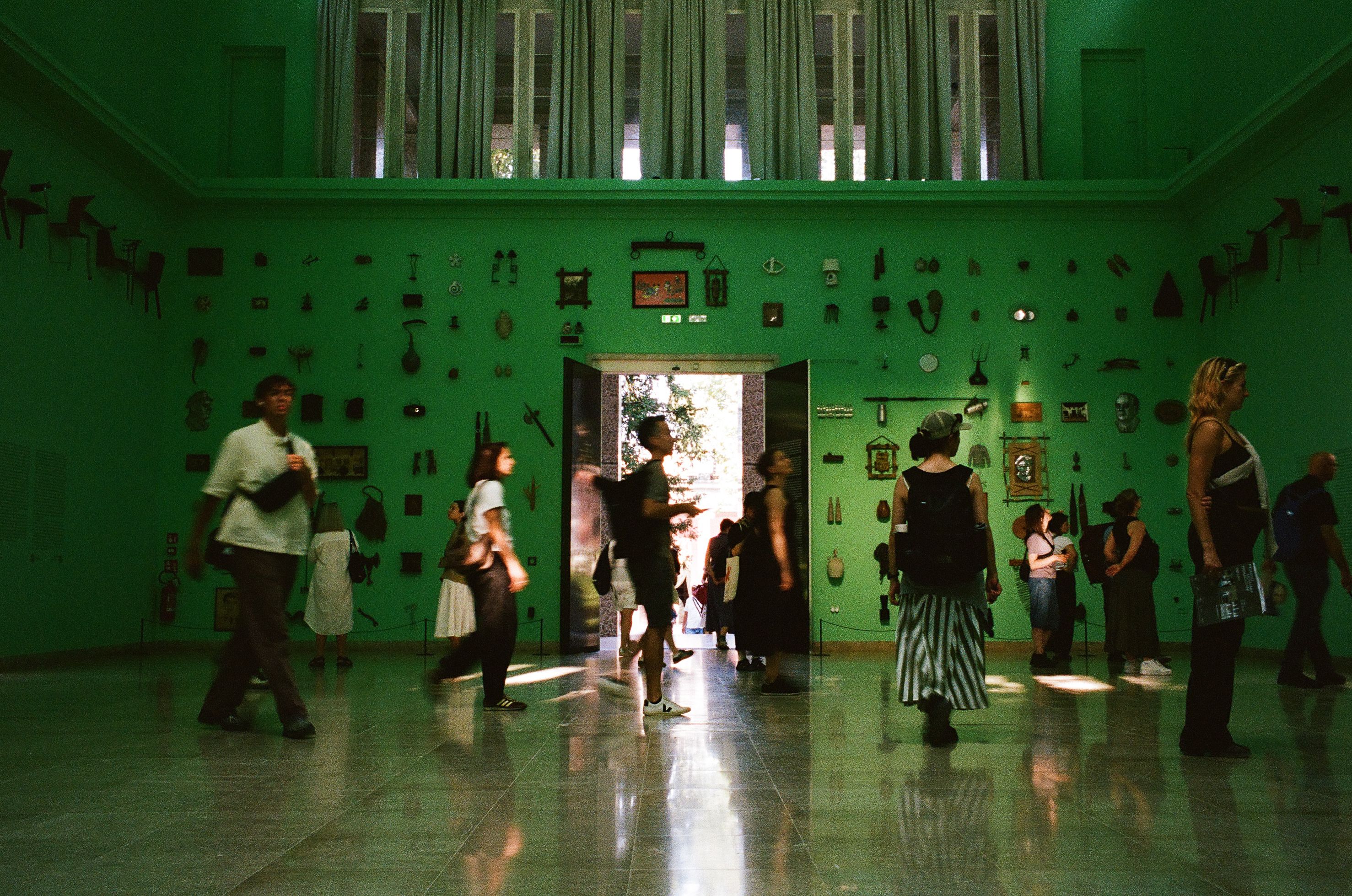 Observing the observers — visitors moving through the green-lit German Pavilion.