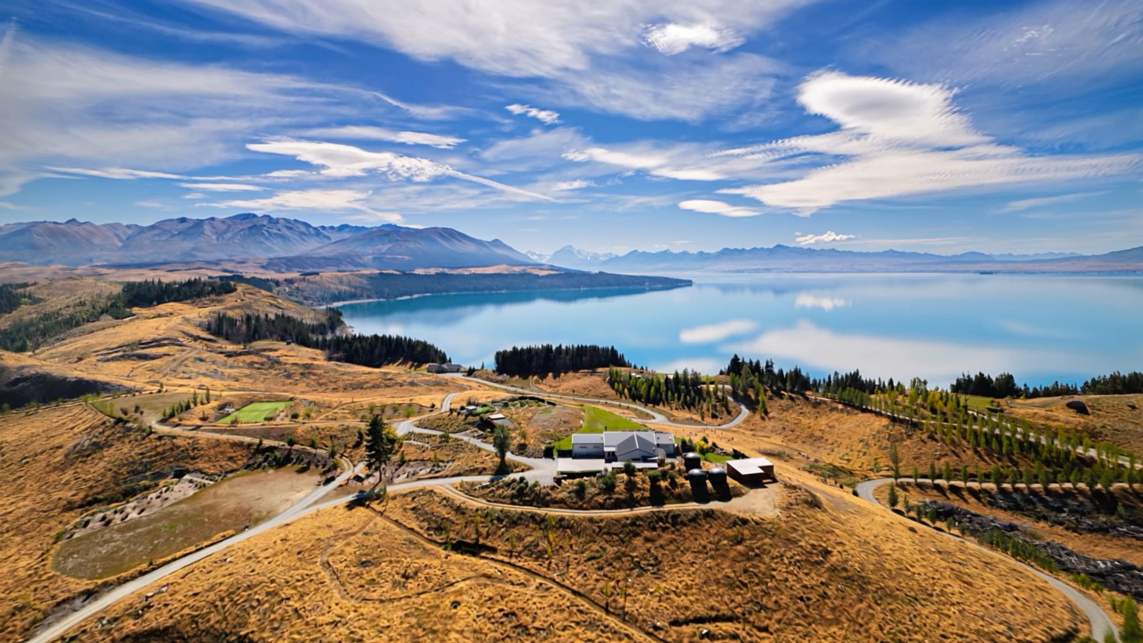 Aerial view over golden tussock hills and the turquoise water of Lake Pukaki, with the Southern Alps beyond, New Zealand