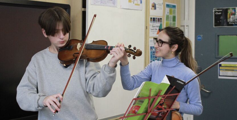 Two students playing string instruments together.