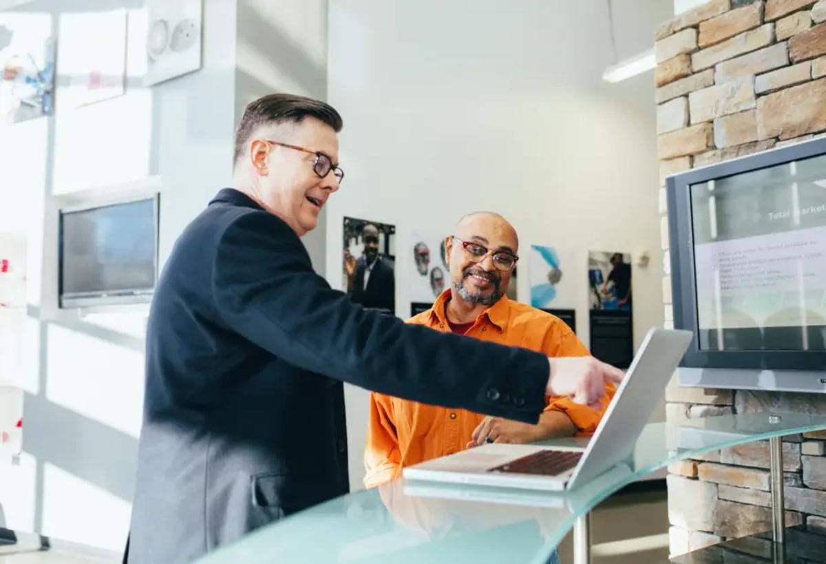 Two business professionals collaborating on a laptop to explore Zlendo Realty AI software sales and consulting opportunities