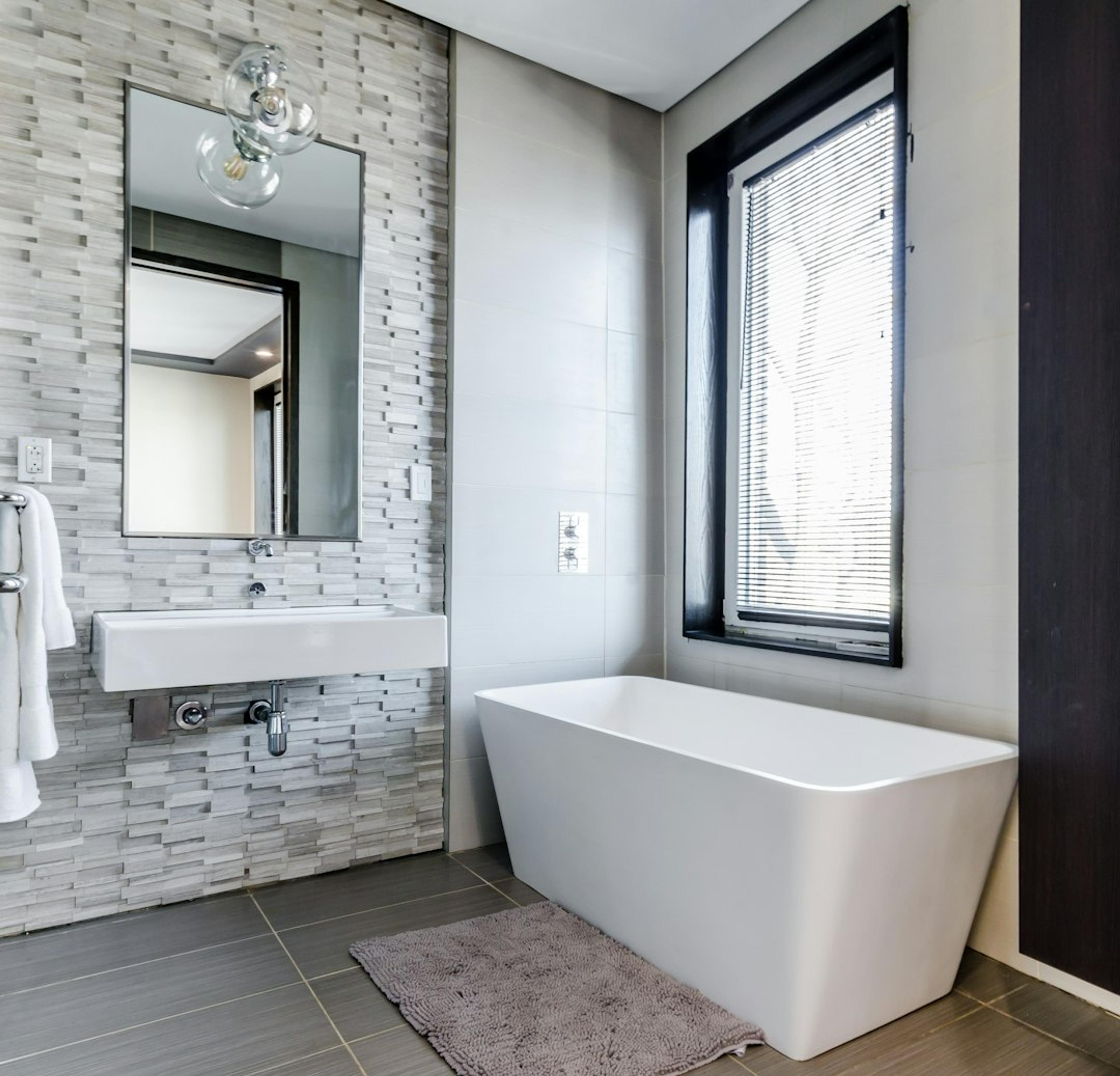 Freestanding tub against a stone tile accent wall with black-framed window