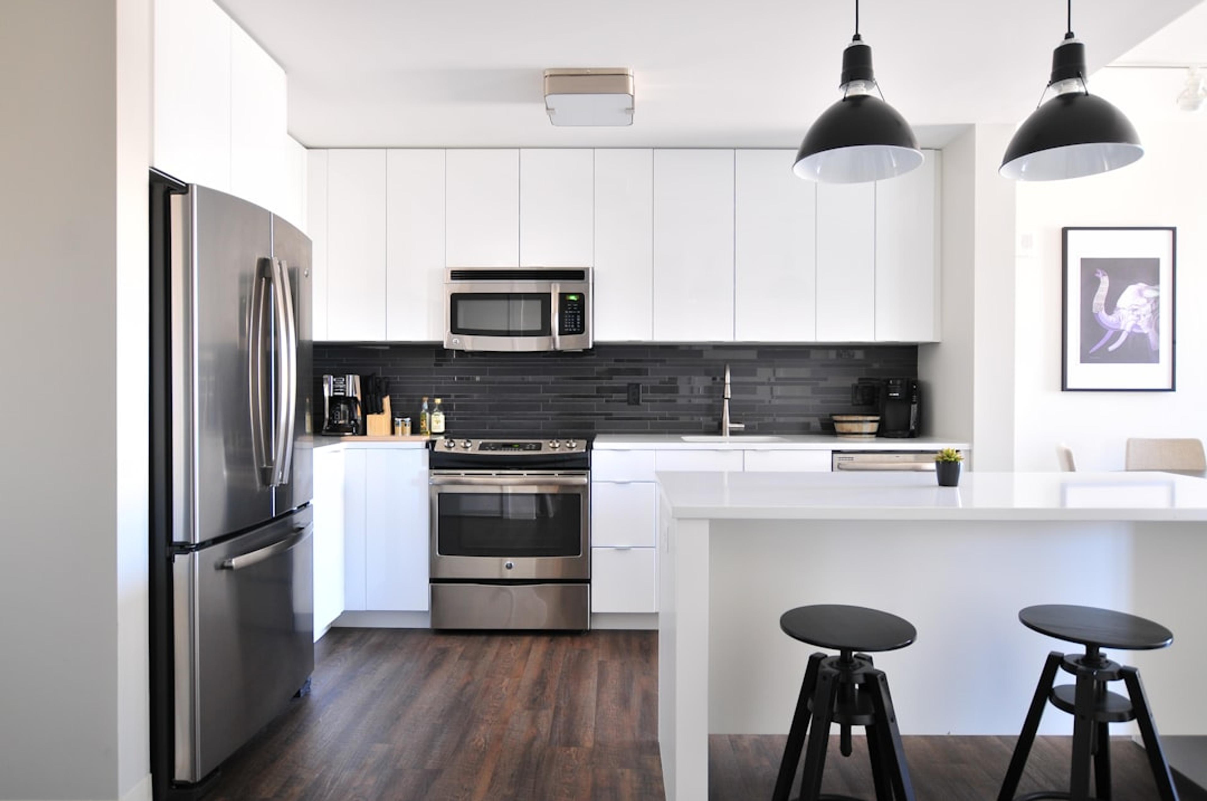 White cabinets with black backsplash wall, white island, and black dome pendants